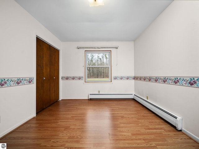 unfurnished room featuring wood finished floors, baseboards, and a baseboard radiator