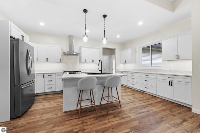 kitchen featuring dark wood-type flooring, freestanding refrigerator, wall chimney range hood, and a sink