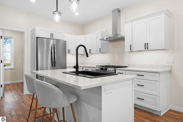 kitchen with an island with sink, a sink, a kitchen breakfast bar, freestanding refrigerator, and wall chimney range hood