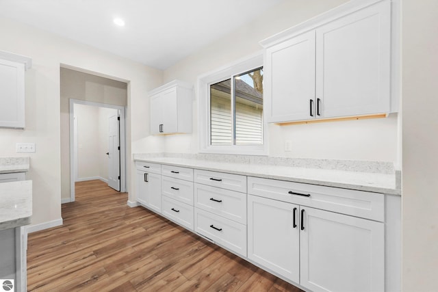 kitchen featuring light wood-style flooring, light stone counters, recessed lighting, white cabinets, and baseboards