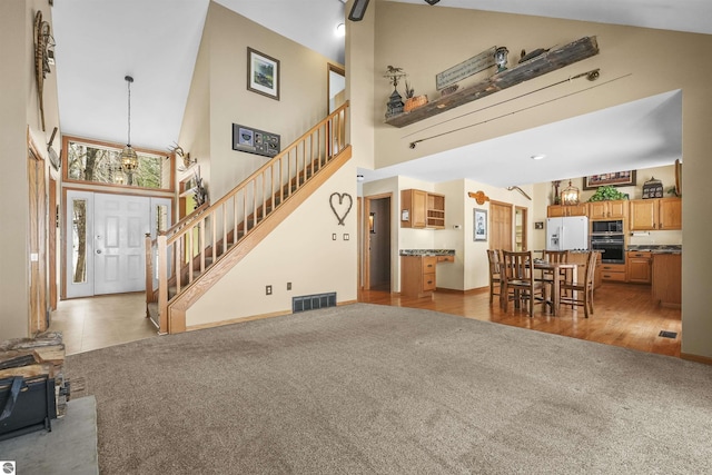 carpeted living room with stairs, visible vents, and high vaulted ceiling