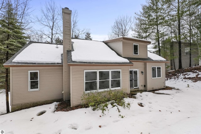 snow covered back of property featuring a chimney