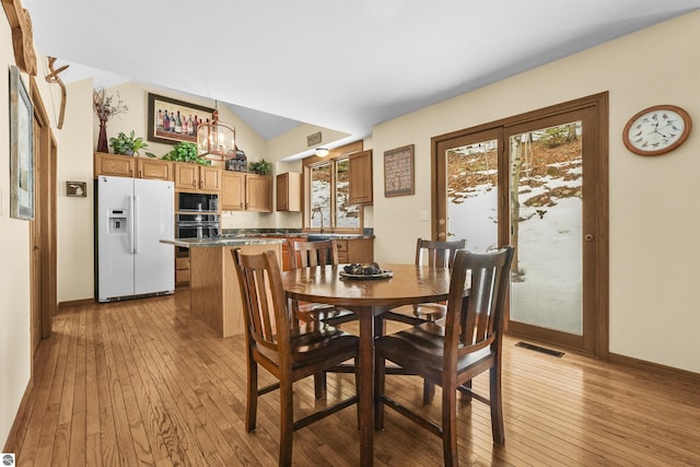 dining room featuring visible vents, baseboards, lofted ceiling, and light wood-style floors