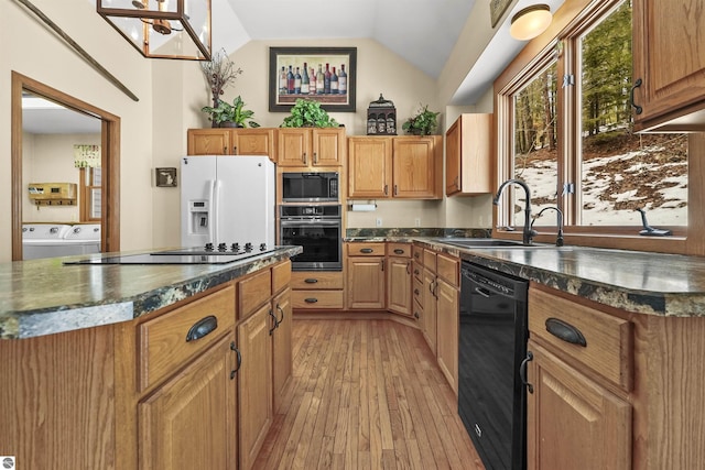 kitchen with washing machine and clothes dryer, lofted ceiling, light wood-style flooring, black appliances, and a sink