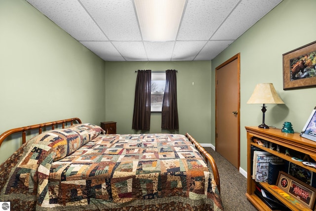 carpeted bedroom featuring a drop ceiling and baseboards