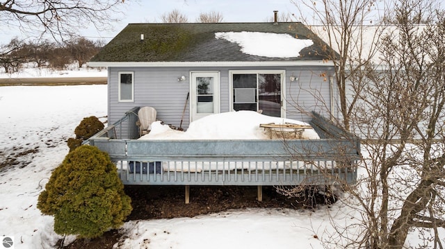 snow covered rear of property with roof with shingles and a wooden deck