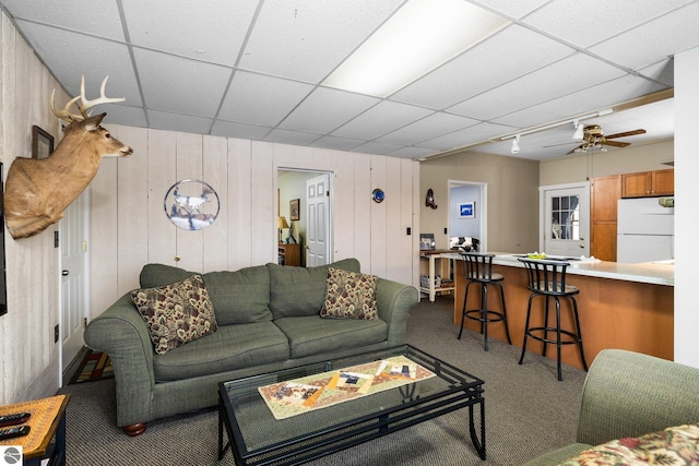 carpeted living area with a drop ceiling and a ceiling fan