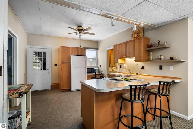 kitchen featuring black microwave, light carpet, brown cabinetry, and freestanding refrigerator