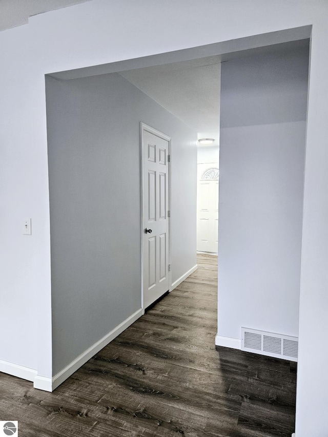 hall with dark wood-style floors, visible vents, and baseboards