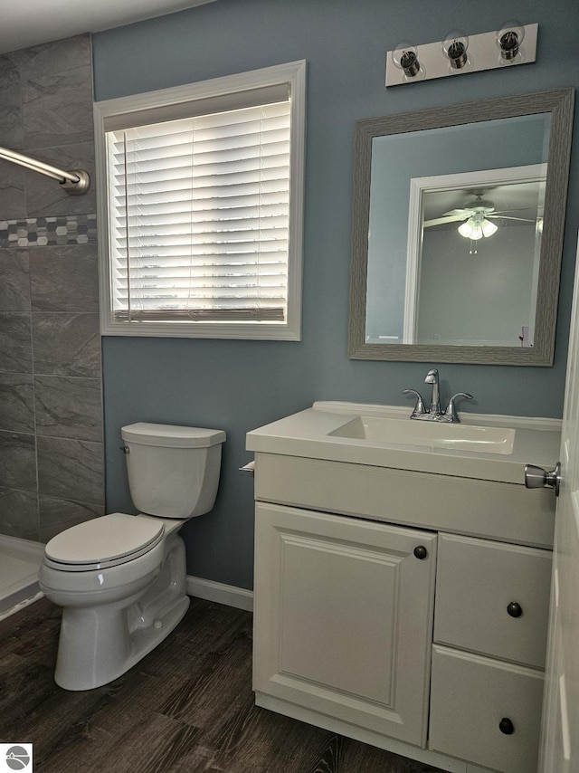 bathroom featuring baseboards, toilet, tiled shower, wood finished floors, and vanity