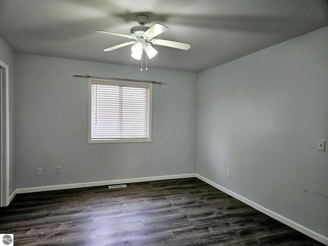 spare room featuring a ceiling fan, visible vents, dark wood-style floors, and baseboards