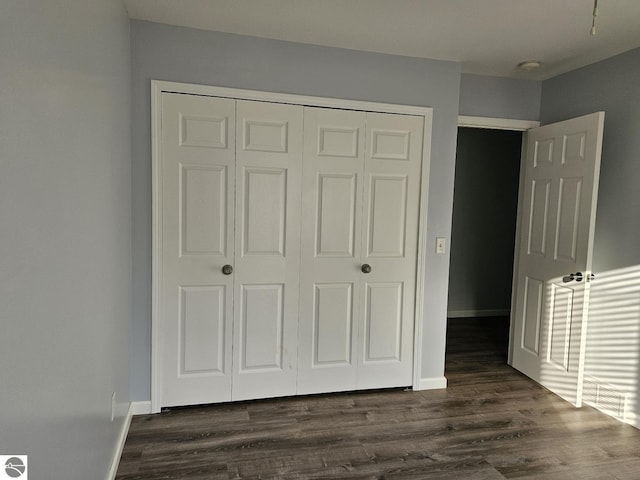 unfurnished bedroom featuring dark wood-type flooring, baseboards, and a closet