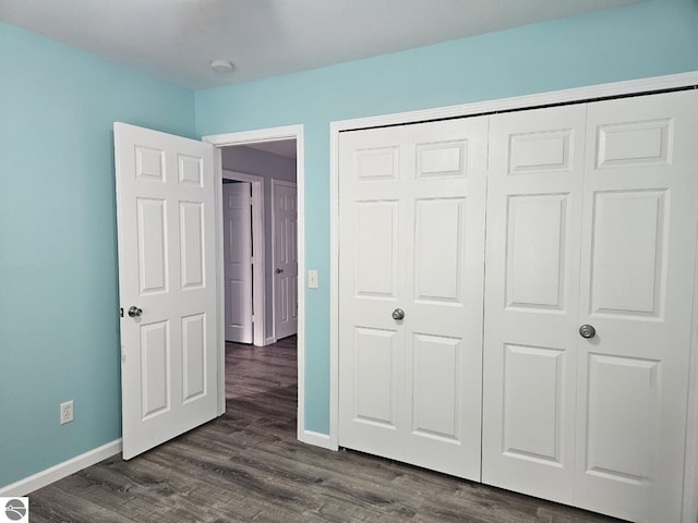 unfurnished bedroom featuring a closet, baseboards, and dark wood-style flooring