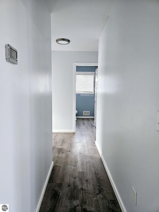 hall with visible vents, baseboards, and wood finished floors