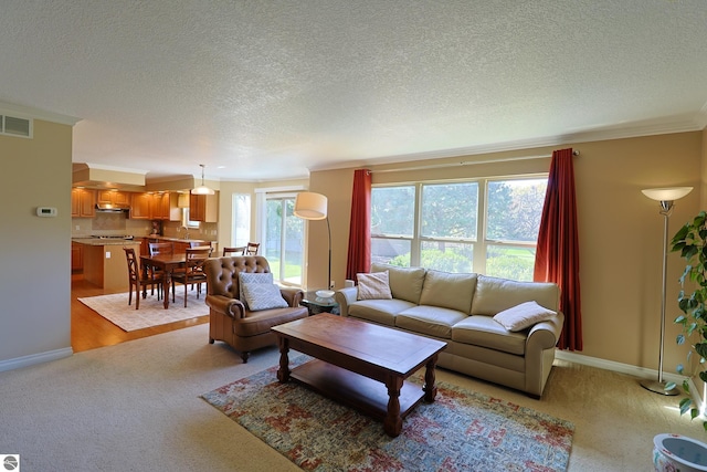 living area with visible vents, baseboards, light colored carpet, ornamental molding, and a textured ceiling