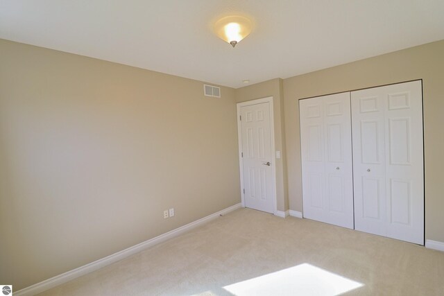 unfurnished bedroom featuring baseboards, visible vents, a closet, and light carpet