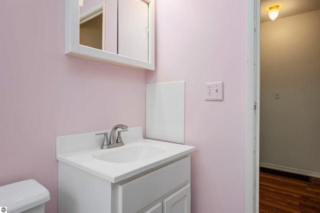 half bath with toilet, wood finished floors, and vanity