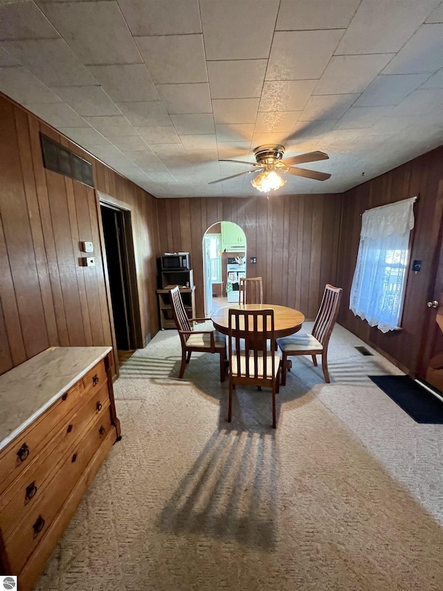 dining area featuring wooden walls, visible vents, light colored carpet, arched walkways, and a ceiling fan