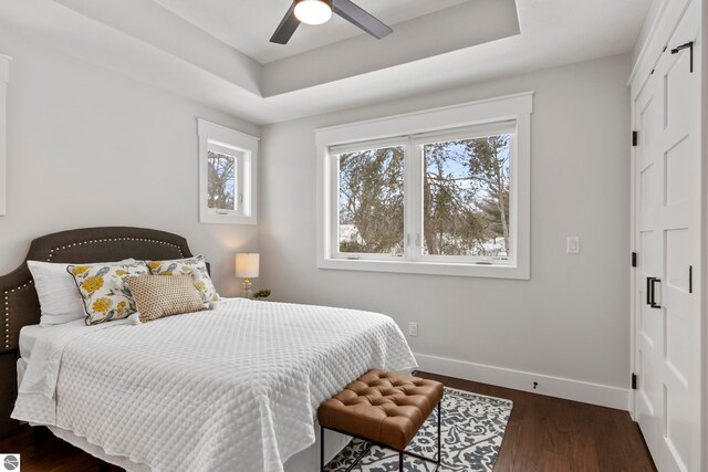 bedroom with ceiling fan, a raised ceiling, baseboards, and dark wood-style flooring