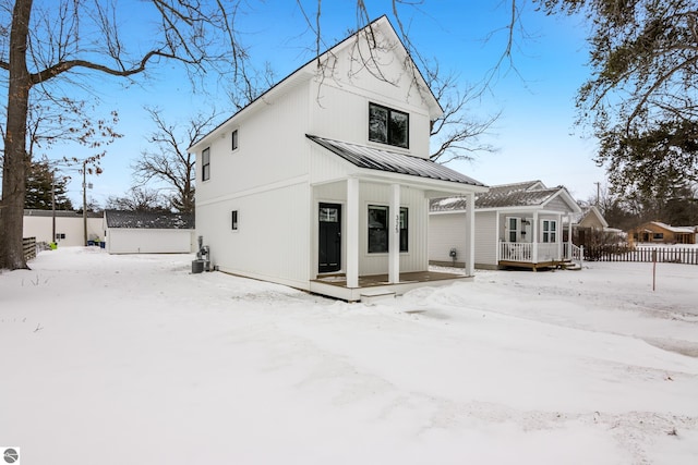 snow covered rear of property featuring fence and metal roof