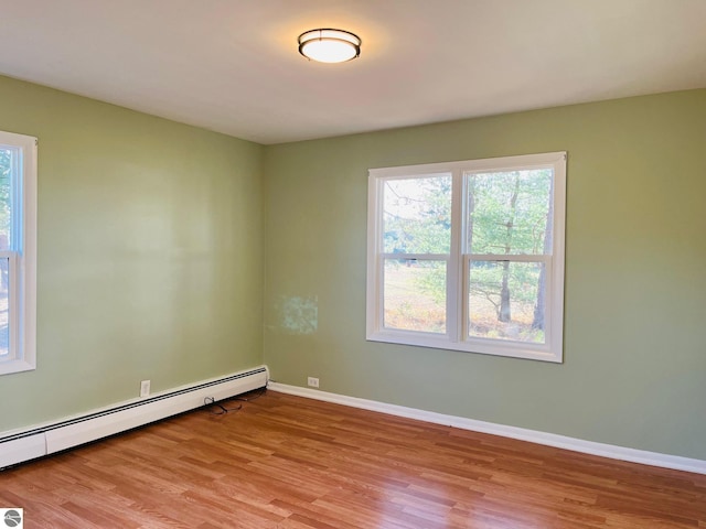 empty room with a baseboard heating unit, plenty of natural light, baseboards, and light wood-style flooring