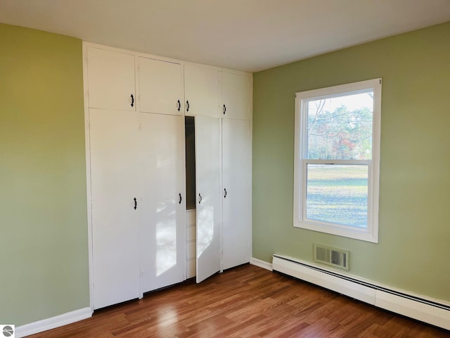 unfurnished bedroom featuring wood finished floors, a closet, baseboard heating, and baseboards