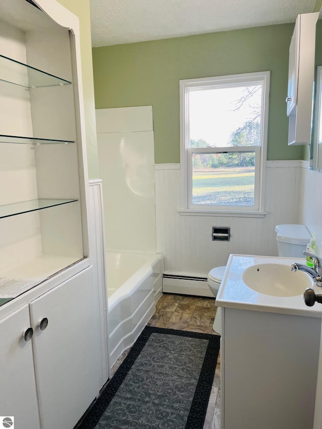 bathroom featuring baseboard heating, wainscoting, a textured ceiling, and toilet