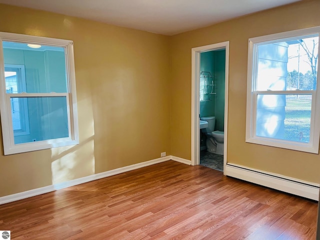 unfurnished room with a baseboard heating unit, baseboards, and light wood finished floors