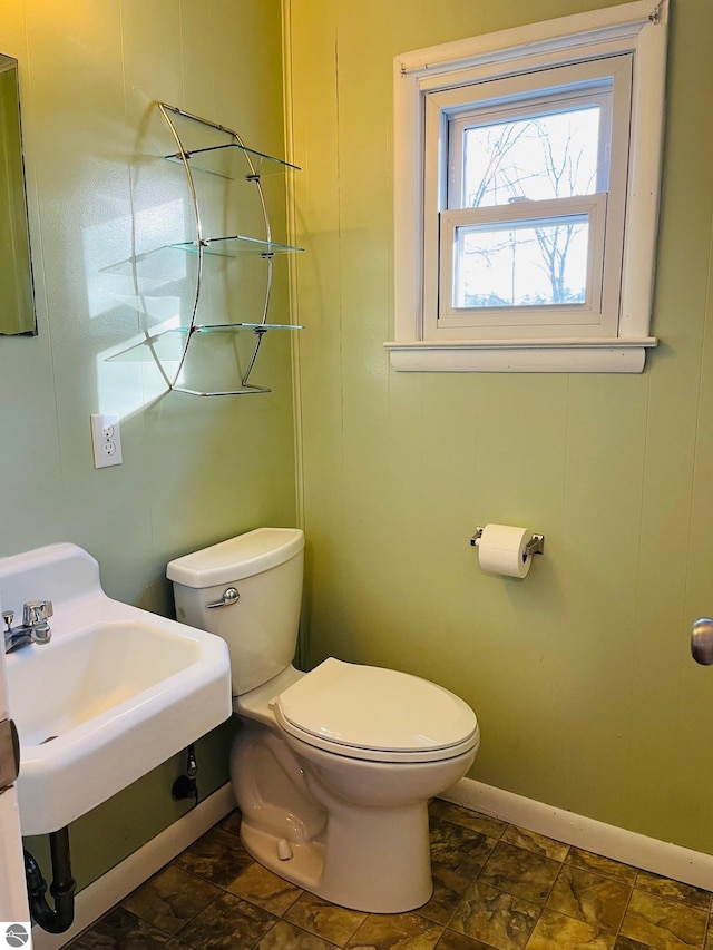 bathroom featuring toilet, stone finish flooring, and baseboards