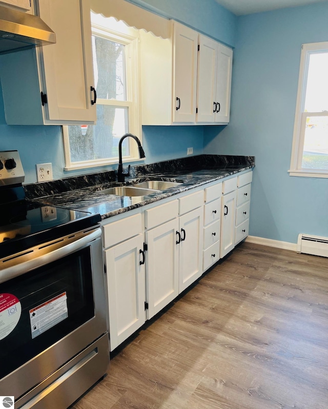 kitchen featuring under cabinet range hood, dark stone countertops, stainless steel electric range, white cabinets, and a sink