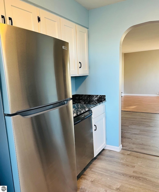 kitchen featuring arched walkways, light wood-style floors, appliances with stainless steel finishes, and white cabinetry