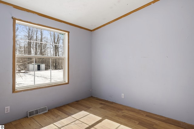 spare room with a wealth of natural light, visible vents, wood finished floors, and crown molding