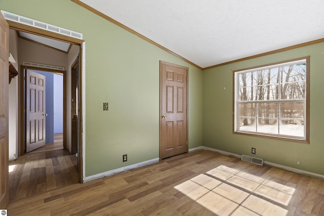 unfurnished bedroom with visible vents, wood finished floors, baseboards, crown molding, and lofted ceiling