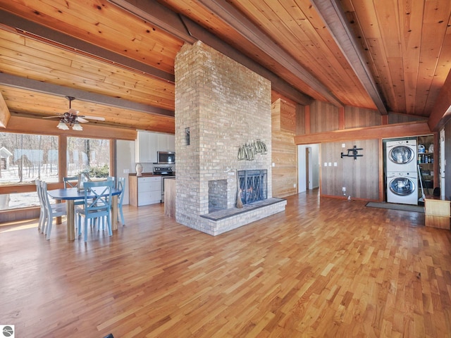 unfurnished living room with a brick fireplace, vaulted ceiling with beams, wooden ceiling, light wood-style floors, and stacked washer / drying machine