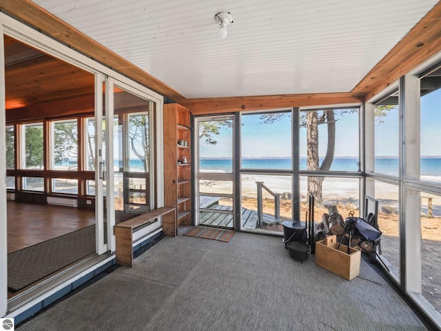 unfurnished sunroom featuring a view of the beach, a water view, and a wealth of natural light