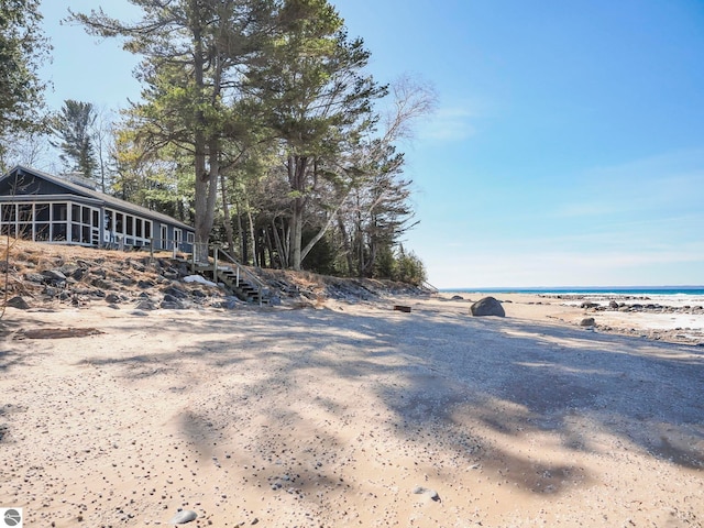 view of yard with stairway, a water view, a sunroom, and a beach view