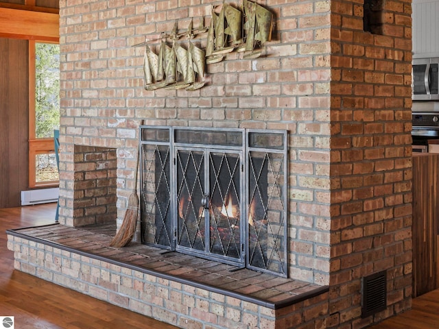 room details featuring visible vents, stainless steel microwave, a brick fireplace, wood finished floors, and stove