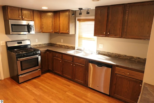 kitchen with dark countertops, appliances with stainless steel finishes, light wood-style floors, and a sink