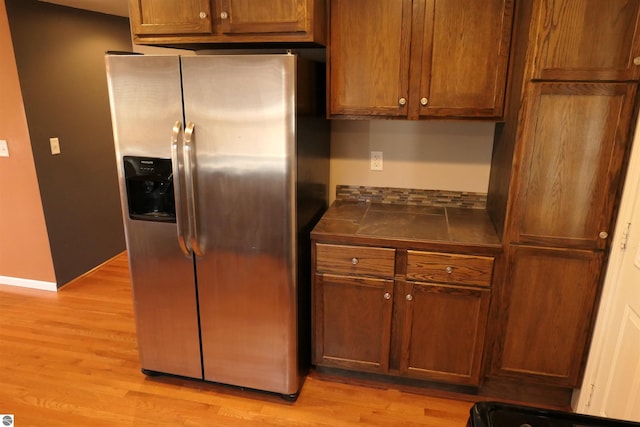 kitchen featuring brown cabinetry, light wood-style flooring, baseboards, and stainless steel refrigerator with ice dispenser