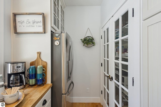 interior space with wood finished floors, baseboards, wooden counters, stainless steel fridge with ice dispenser, and glass insert cabinets