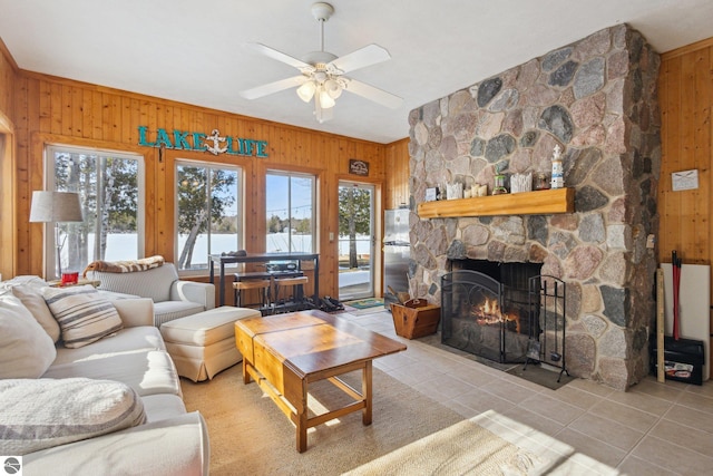 living area featuring light tile patterned floors, wood walls, a fireplace, and ceiling fan