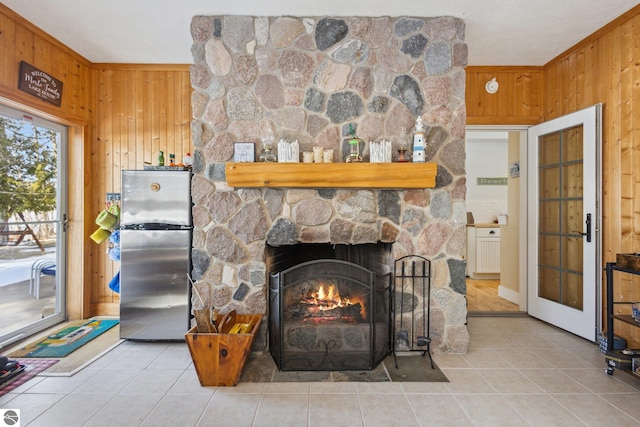 interior details featuring a stone fireplace, wood walls, crown molding, and freestanding refrigerator