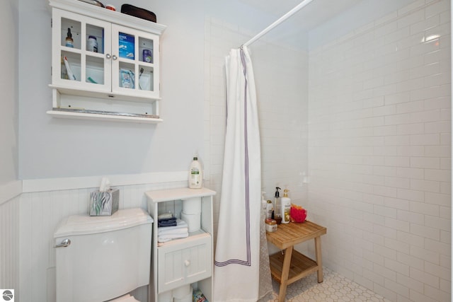 full bath featuring a tile shower, wainscoting, tile patterned floors, and toilet