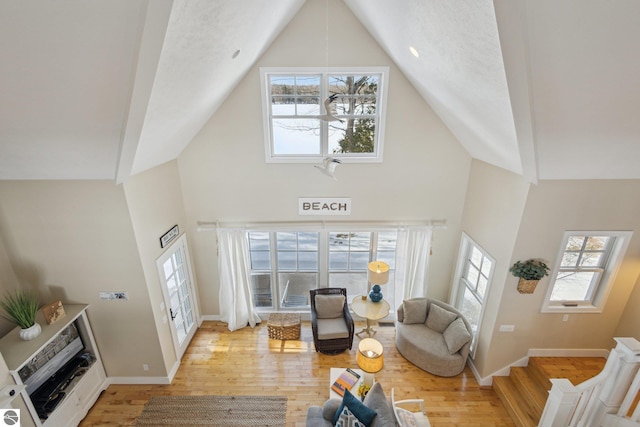 living room with light wood-style flooring, high vaulted ceiling, and baseboards