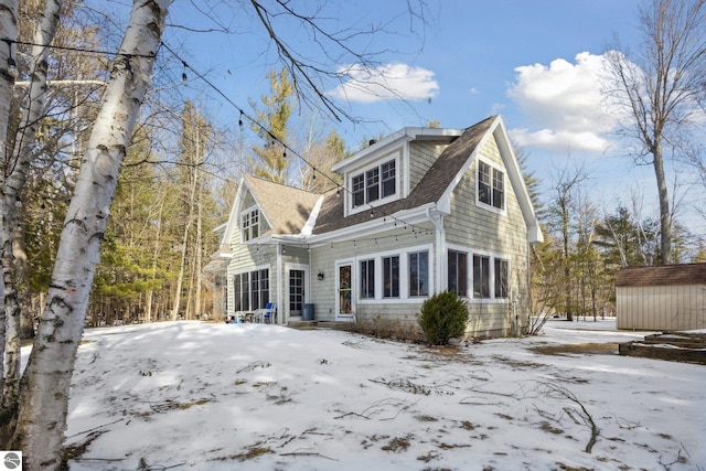 snow covered rear of property featuring a storage unit, an outdoor structure, and roof with shingles