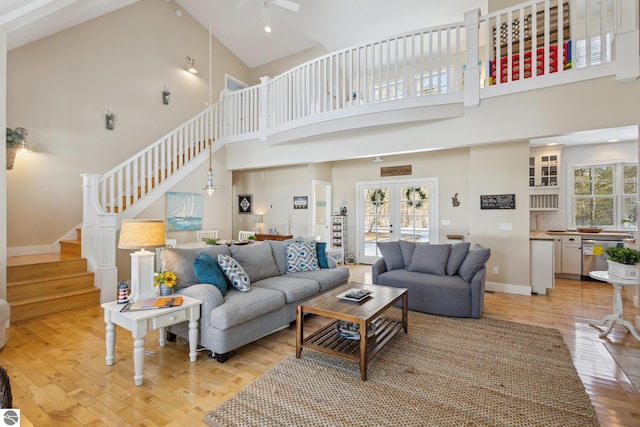 living room featuring baseboards, high vaulted ceiling, stairs, french doors, and light wood-type flooring