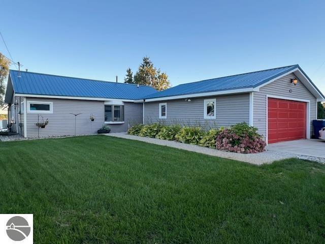 back of house featuring a yard, a garage, metal roof, and driveway