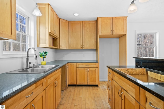 kitchen featuring dark stone countertops, light wood-style flooring, pendant lighting, and a sink