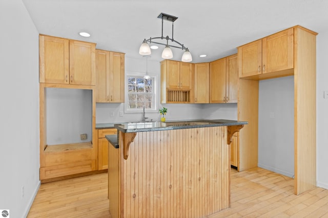 kitchen featuring a sink, dark countertops, a breakfast bar, and light wood-style flooring