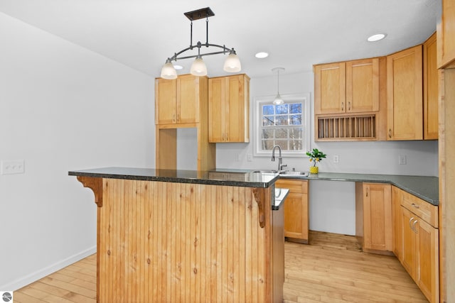 kitchen with light wood finished floors, a kitchen island, a sink, pendant lighting, and a kitchen bar